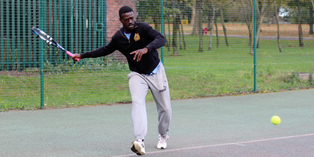 Tennis coach about to strike a tennis ball with his racquet.