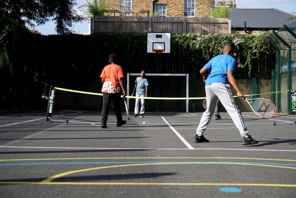 Four boys playing doubles tennis on a multi-purpose hard court